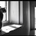 Fotografía en blanco y negro de un gato en la ventana observando a una mujer de pie al otro lado de la habitación.