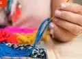 Mano tejiendo con lana azul en un telar de colores con etiqueta 'Free' en la esquina.